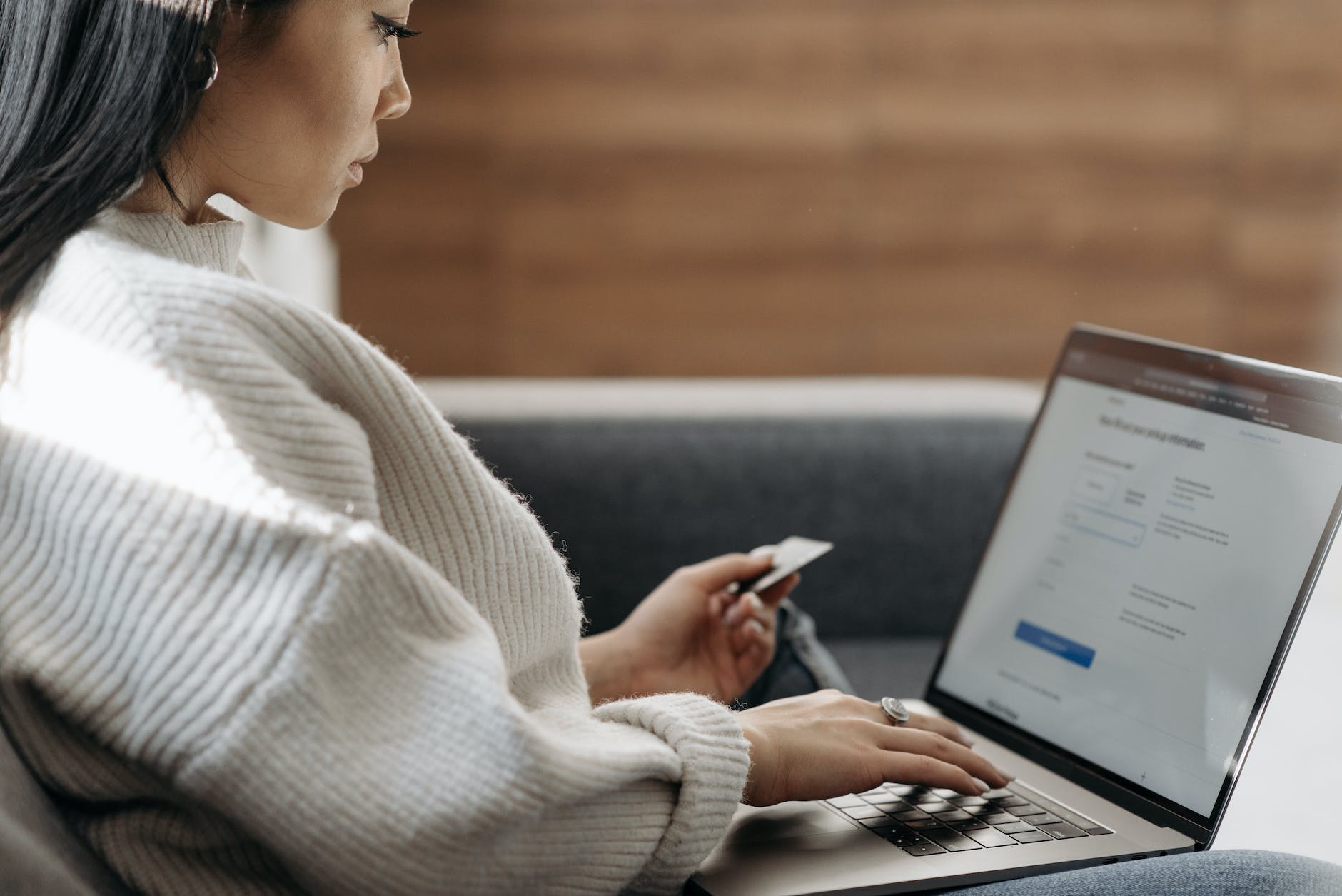 woman in white sweater entering card details into laptop